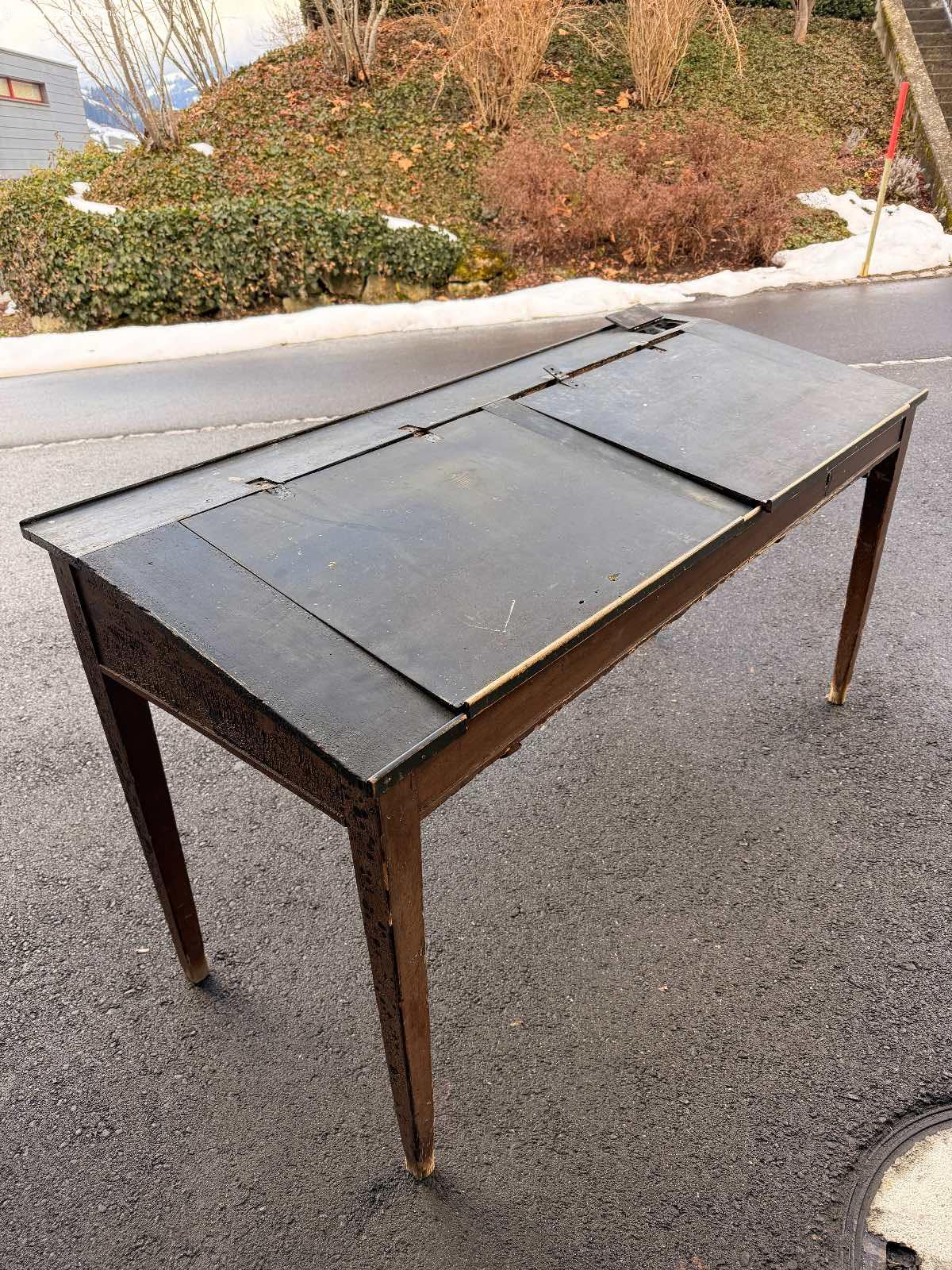 Antike Schulbank / Schultisch ca. 1900-1930 - mit Patina. Originale antike Schulbank aus Holz, vermutlich aus der Zeit ca. 1900-1930. Klassischer Schultisch mit zwei Klappdeckeln und integrierten Ablagefächern, wie sie früher in Schulzimmern verwendet wurden.
Die Tintenloch-Öffnungen sind noch sichtbar.
Der Tisch weist eine wunderschöne, authentische Patina mit altersbedingten Gebrauchsspuren auf. Die schwarze Lackierung ist teilweise stark gekrakelt, was den historischen Charakter unterstreicht.
Zustand:
• Beide originalen Klappdeckel sind vorhanden
• Die Scharniere sind ausgerissen, können jedoch fachgerecht repariert werden
• Holzsubstanz insgesamt stabil
• Alters- und Gebrauchsspuren gemäss Fotos
Ideal als Dekorationsobjekt, für ein Vintage-Interieur, Atelier, Ladenbau oder als Restaurationsprojekt für
Liebhaber alter Schulmöbel.
Masse: ca. 89 x 67 x 160